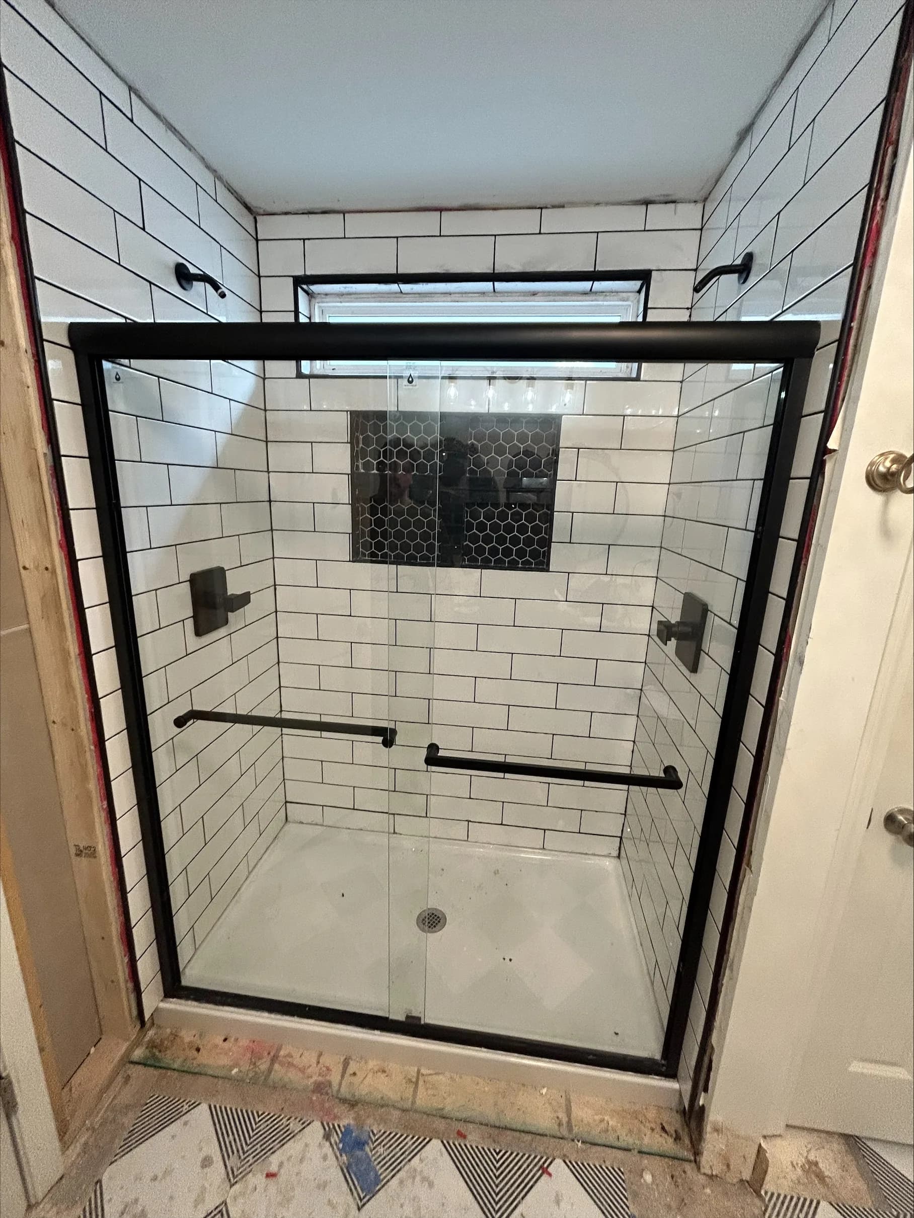 White subway tile shower with black grout, black-framed glass doors, and hexagonal mosaic accent niche