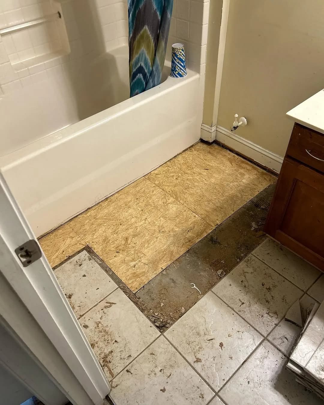 Old tile flooring partially removed exposing plywood subfloor