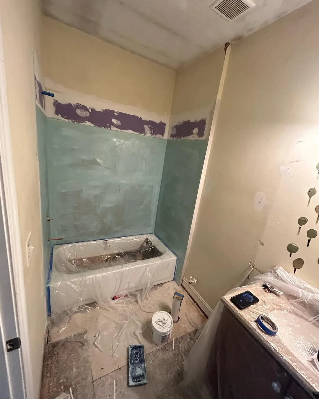 New cement board and waterproofing compound applied around tub area with tub wrapped in plastic