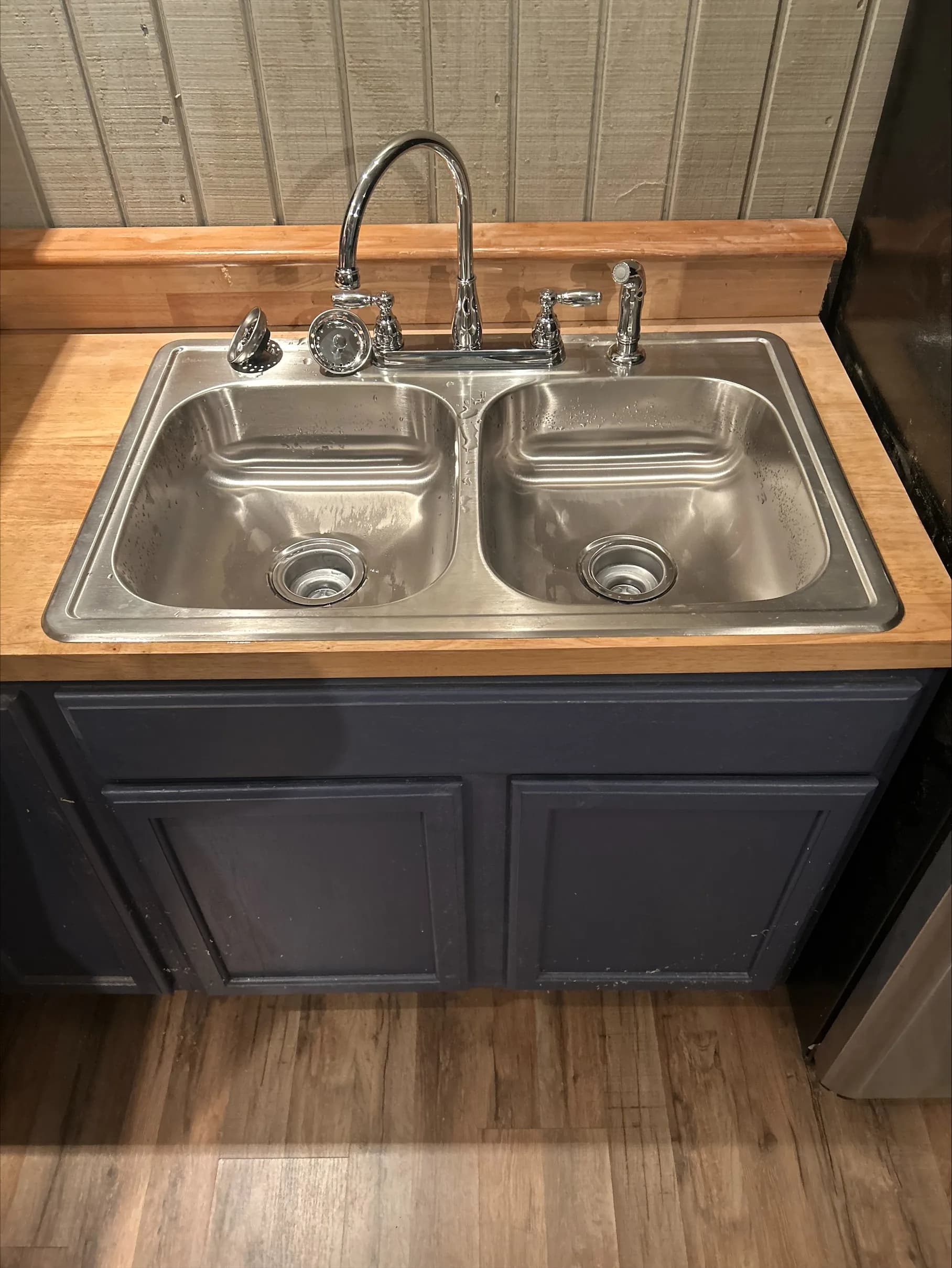 Stainless steel double-basin kitchen sink with chrome high-arc faucet on butcher block countertop